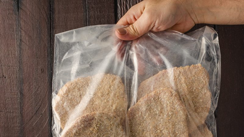 Mano sosteniendo una bolsa de milanesas congeladas Piso Uno en formato mayorista, con la escarcha del congelado visible